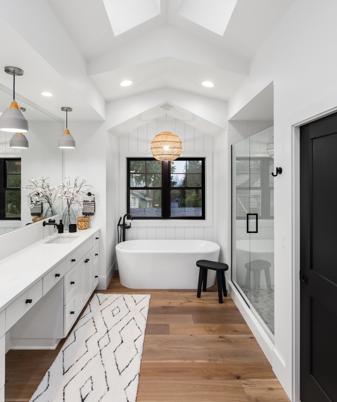 Bathroom in luxury home with double vanity, bathtub, mirror, sinks, shower, and hardwood floor.